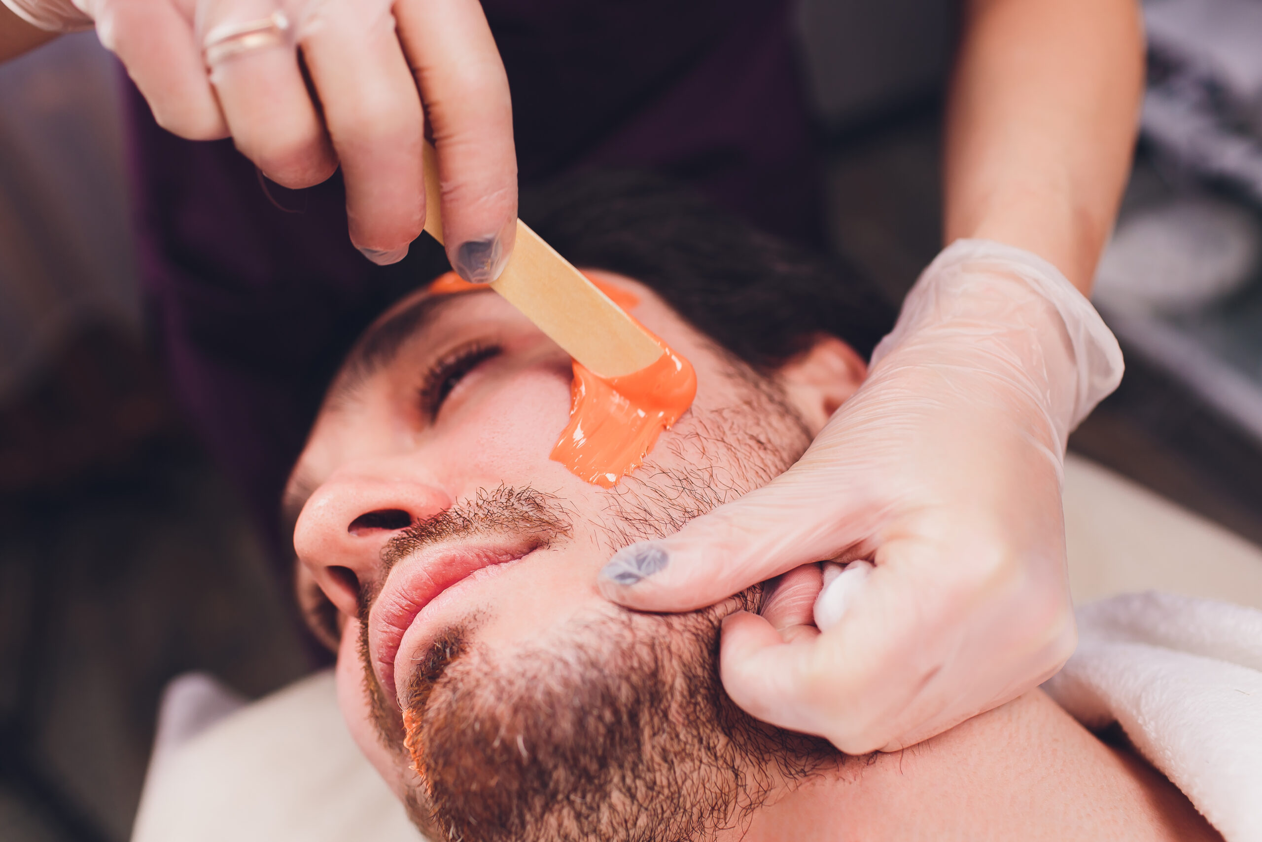 Hair removal. Man's face sugaring epilations beard trimming, yellow color, in cosmetology on the couch